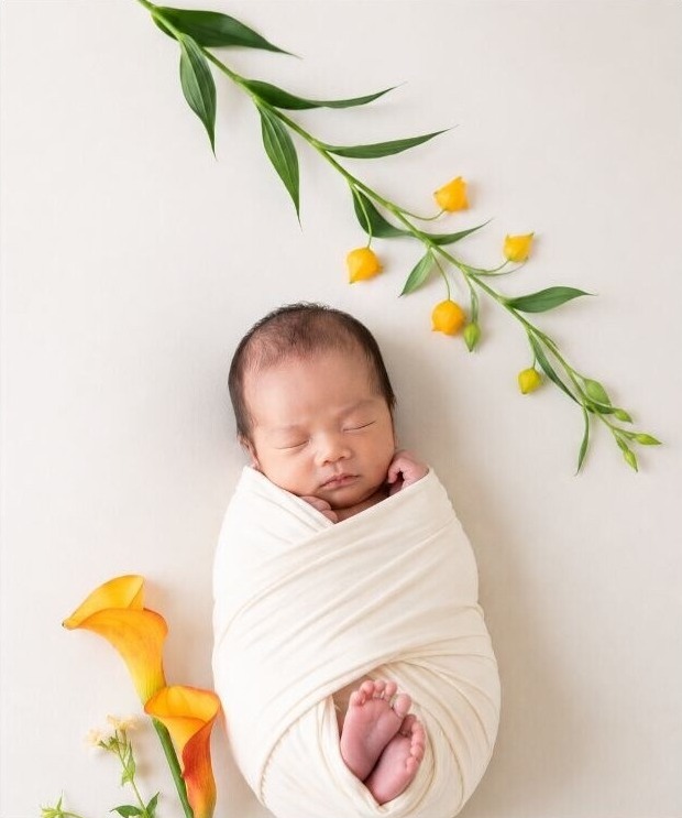 白いおくるみとカラーの花に囲まれた赤ちゃん