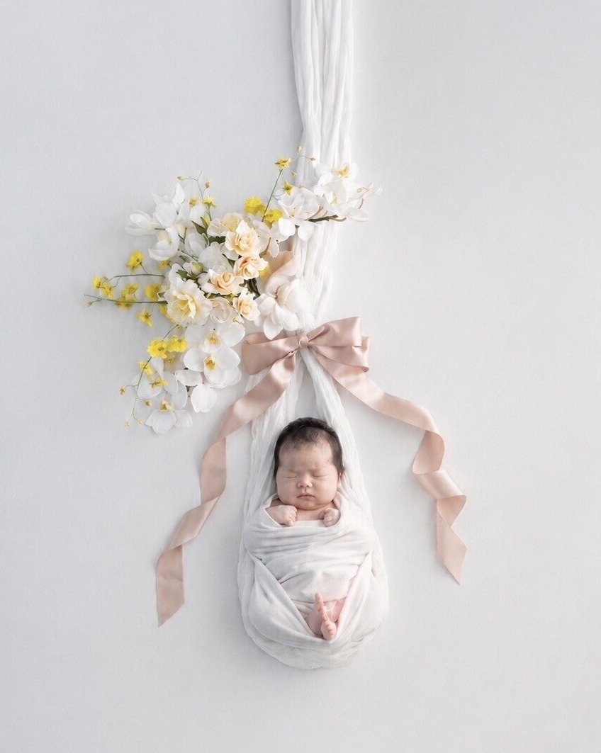 花とリボンで飾られた白いハンモックで眠る赤ちゃん